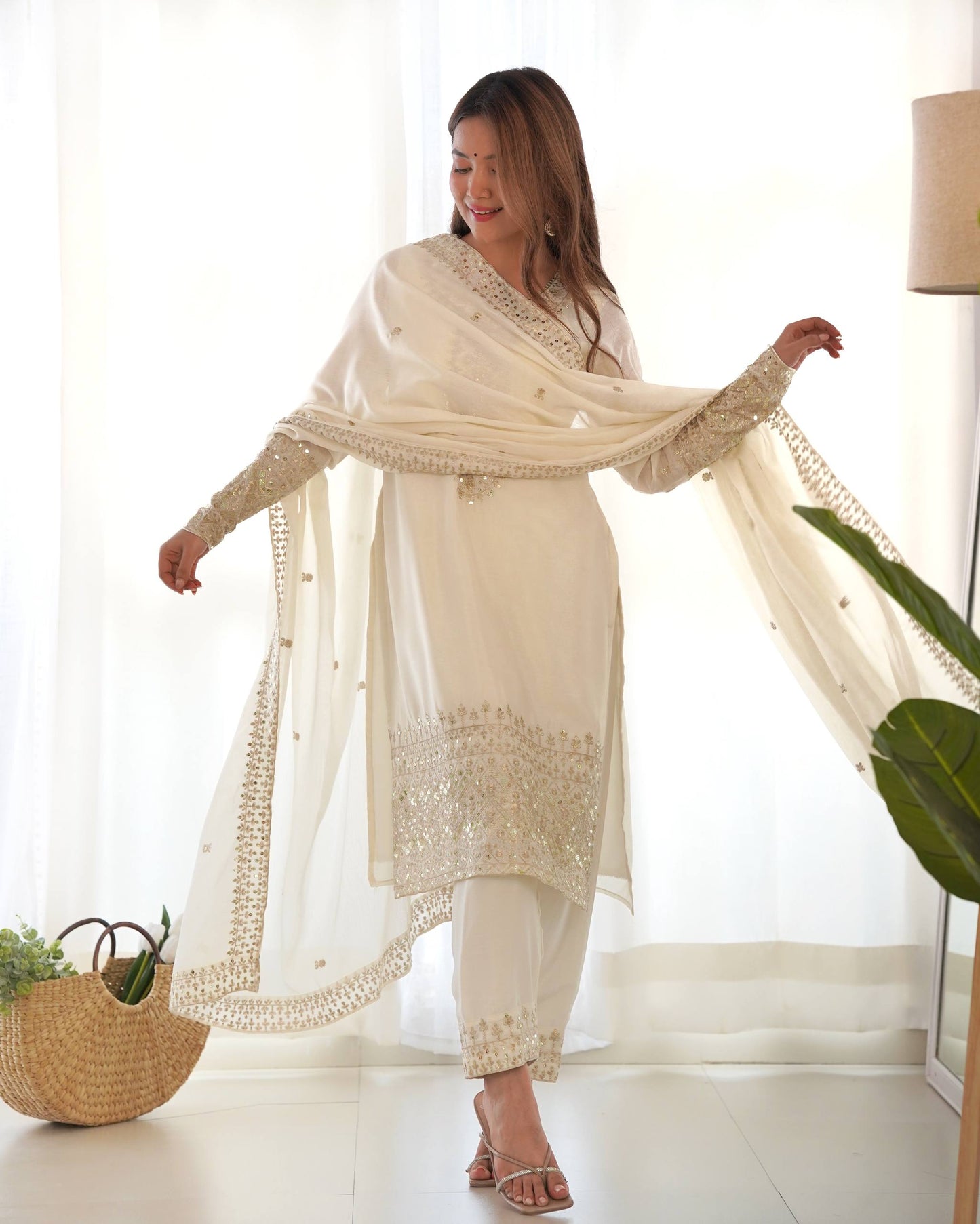 MD-245 This stunning three-piece ensemble captures the essence of sophisticated ethnic wear. Crafted in a luminous off-white silk-blend fabric, the outfit features intricate Zari and mirror-work embroidery that adds a touch of regal shimmer.