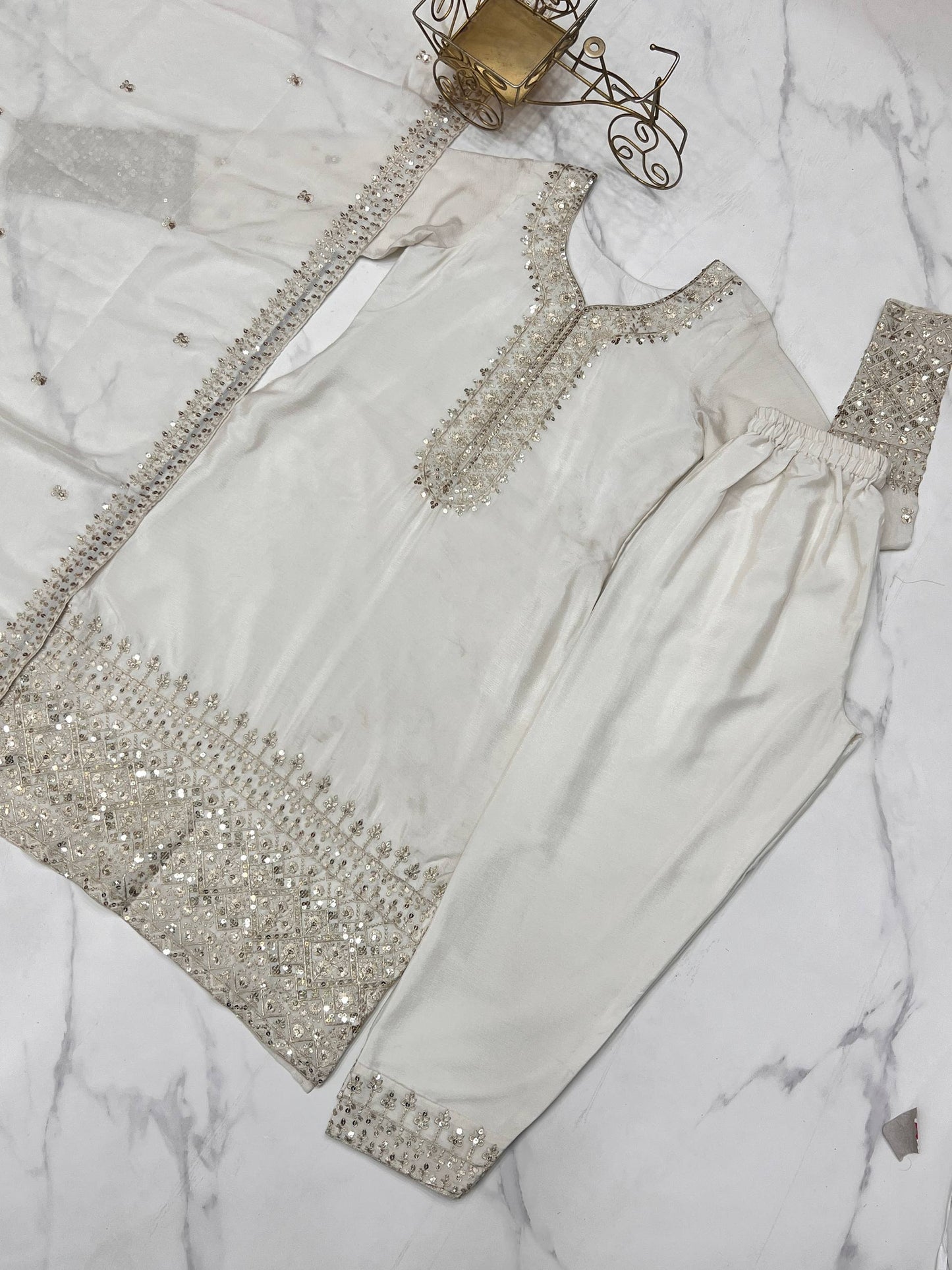 MD-245 This stunning three-piece ensemble captures the essence of sophisticated ethnic wear. Crafted in a luminous off-white silk-blend fabric, the outfit features intricate Zari and mirror-work embroidery that adds a touch of regal shimmer.