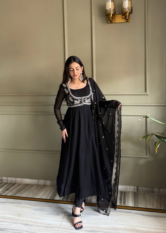 MD-242 This stunning three-piece set features a georgette Anarkali gown, designed with a graceful floor-length flare and a sophisticated round neckline. The ensemble is elevated by a matching sleeveless blouse (or jacket overlay) adorned with i