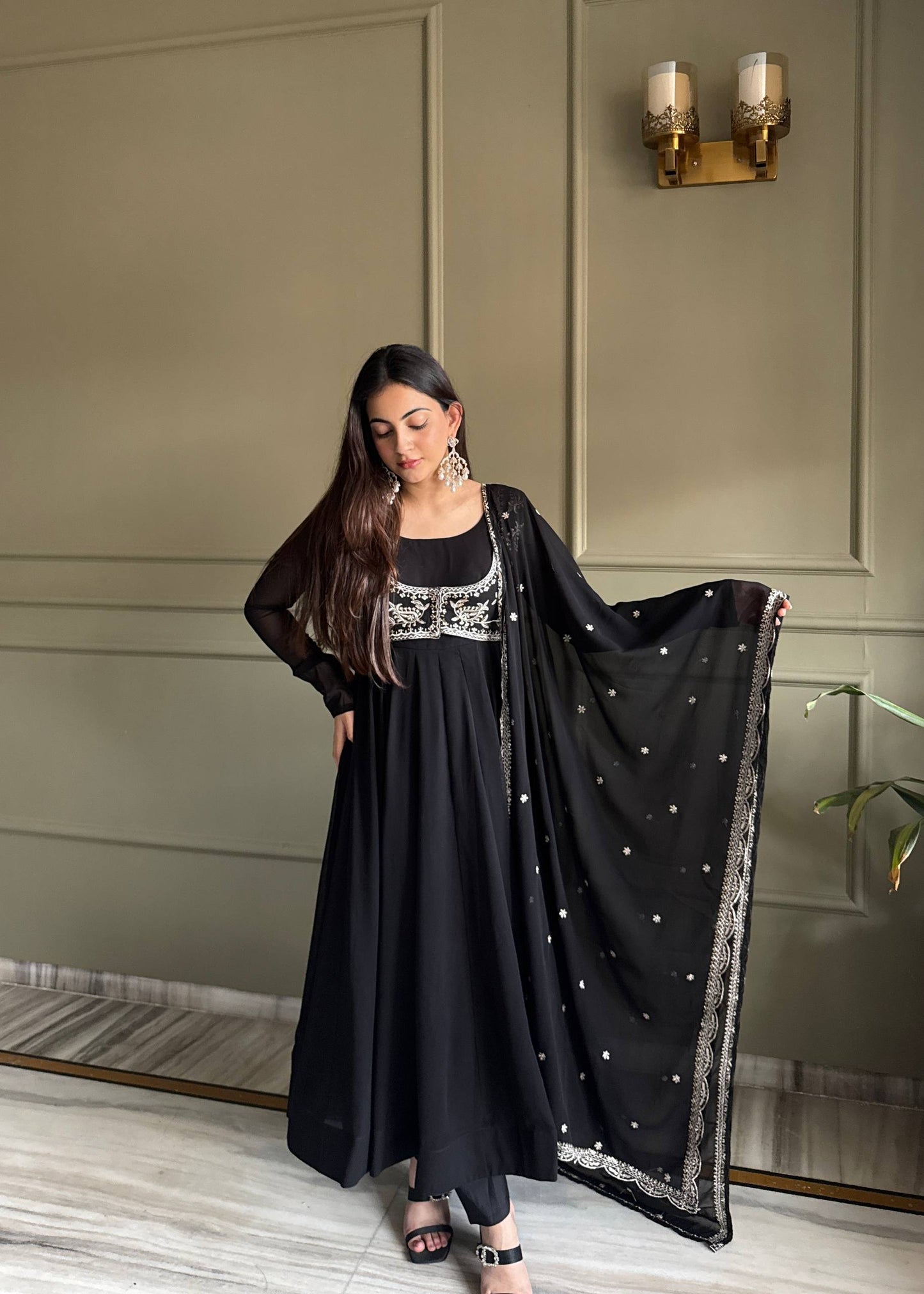 MD-242 This stunning three-piece set features a georgette Anarkali gown, designed with a graceful floor-length flare and a sophisticated round neckline. The ensemble is elevated by a matching sleeveless blouse (or jacket overlay) adorned with i