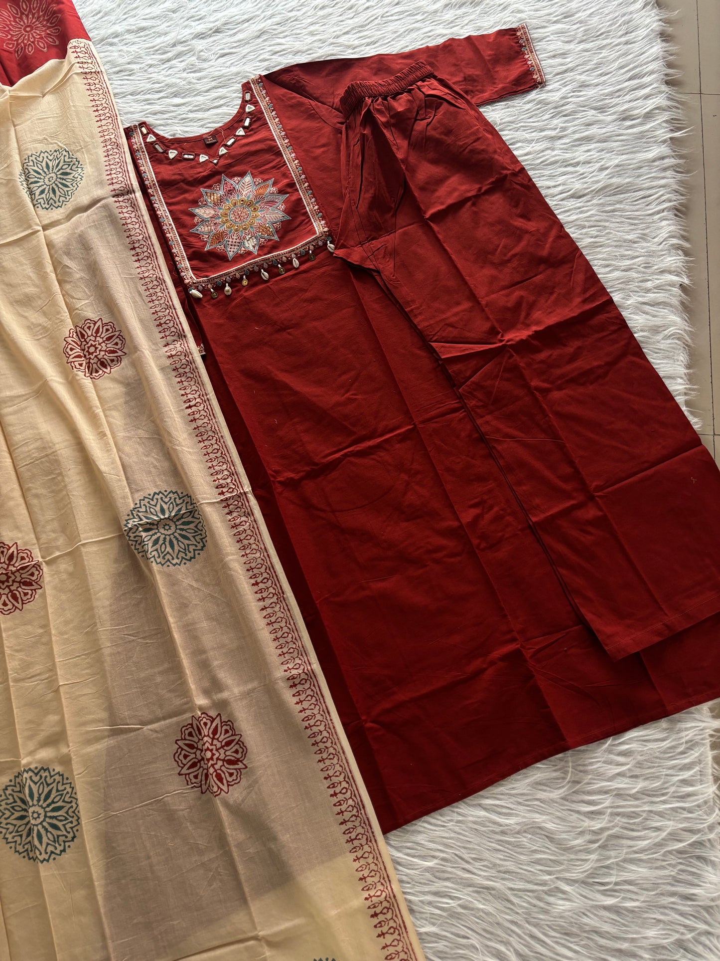 MD-265 This elegant three-piece ethnic set features a deep Kurti and matching trousers, paired with a contrasting cream-colored Dupatta. The ensemble balances rich, solid tones with intricate traditional detailing, making it ideal for festive