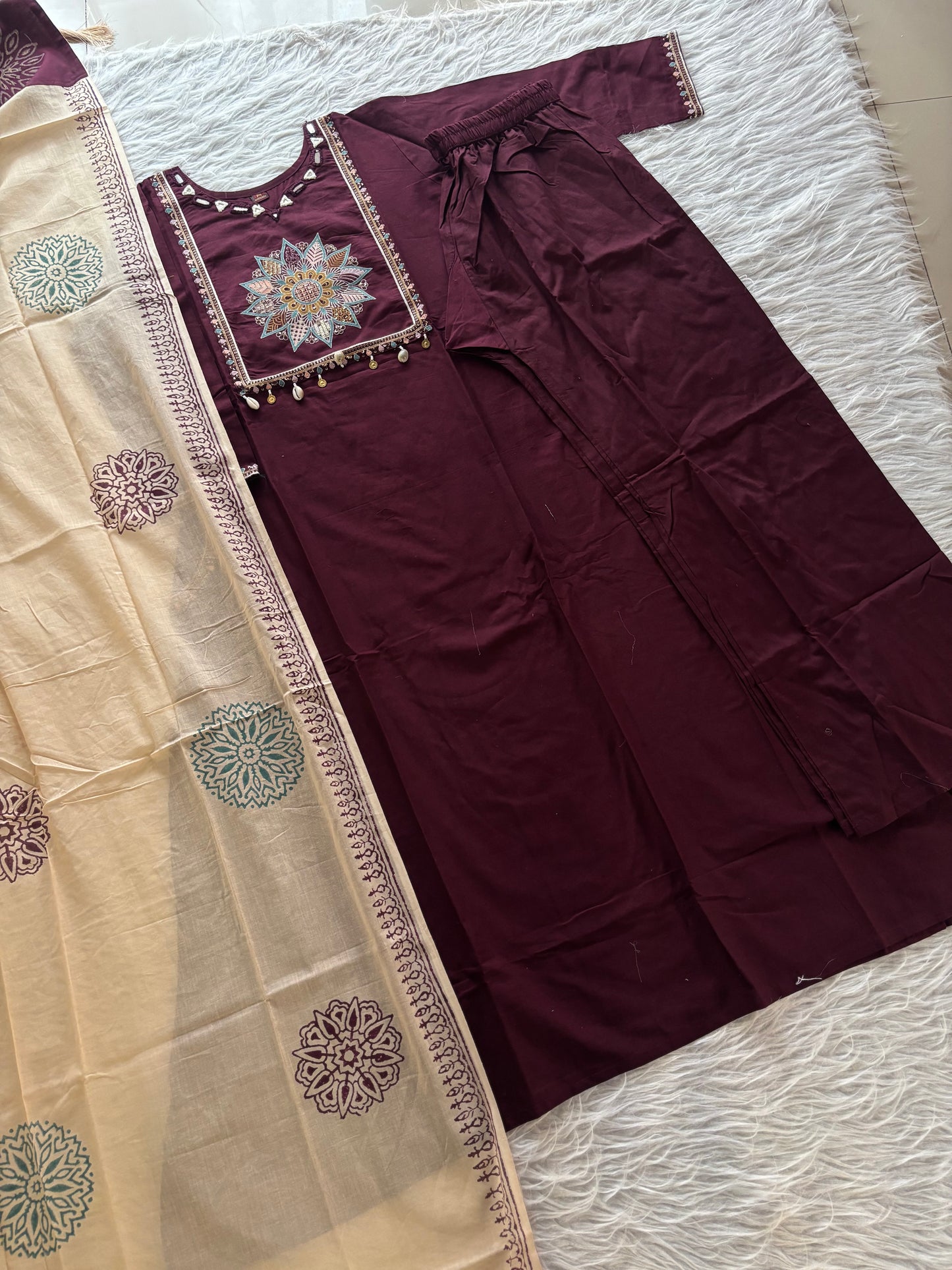 MD-265 This elegant three-piece ethnic set features a deep Kurti and matching trousers, paired with a contrasting cream-colored Dupatta. The ensemble balances rich, solid tones with intricate traditional detailing, making it ideal for festive
